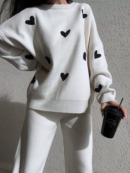 White sweater with black heart patterns worn by a person against a plain background