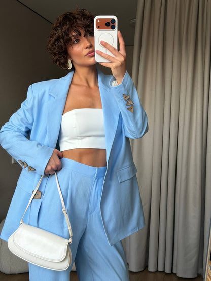 Person wearing a light blue suit with a white top and holding a white handbag indoors.