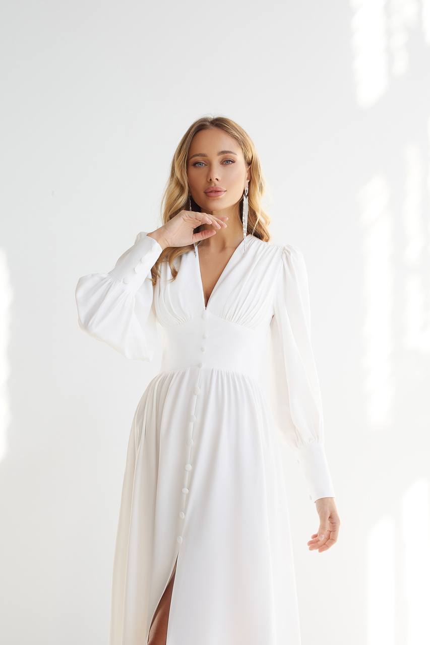 Woman wearing a white dress with long sleeves against a white background