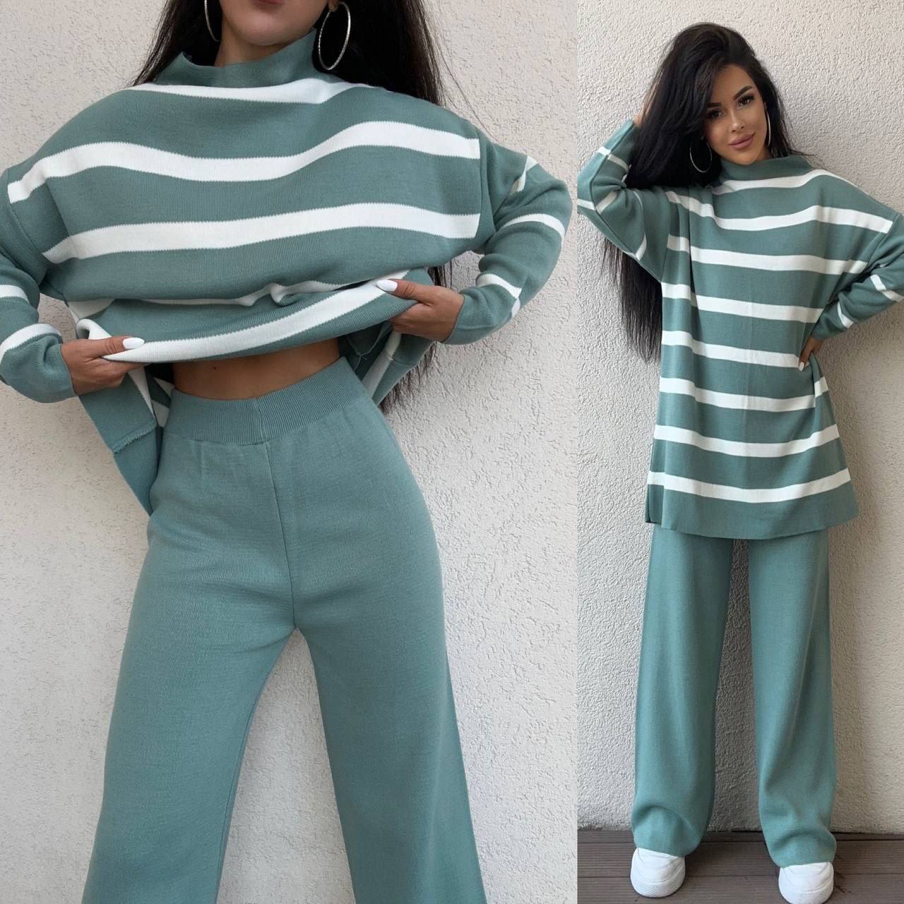 Woman wearing a green and white striped sweater and pants set against a neutral background.