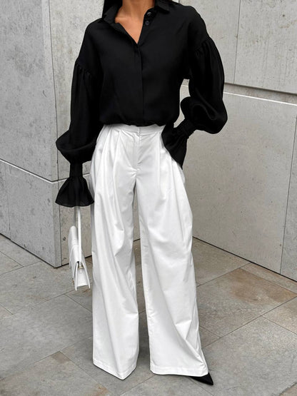 Person wearing a black shirt and white pants against a gray wall.