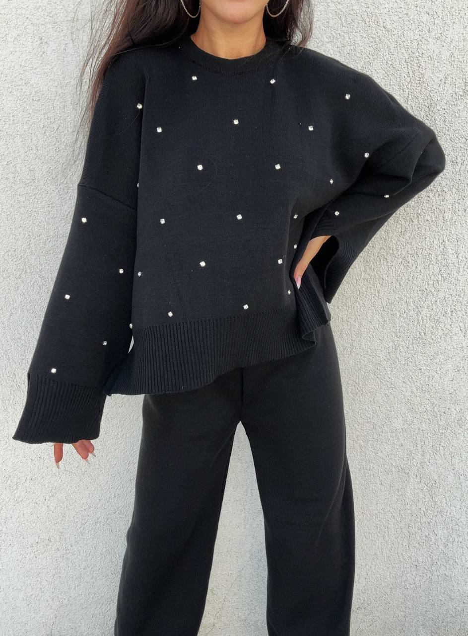 Person wearing a black sweater with white embellishments against a light gray background