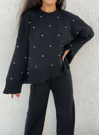 Person wearing a black sweater with white embellishments against a light gray background