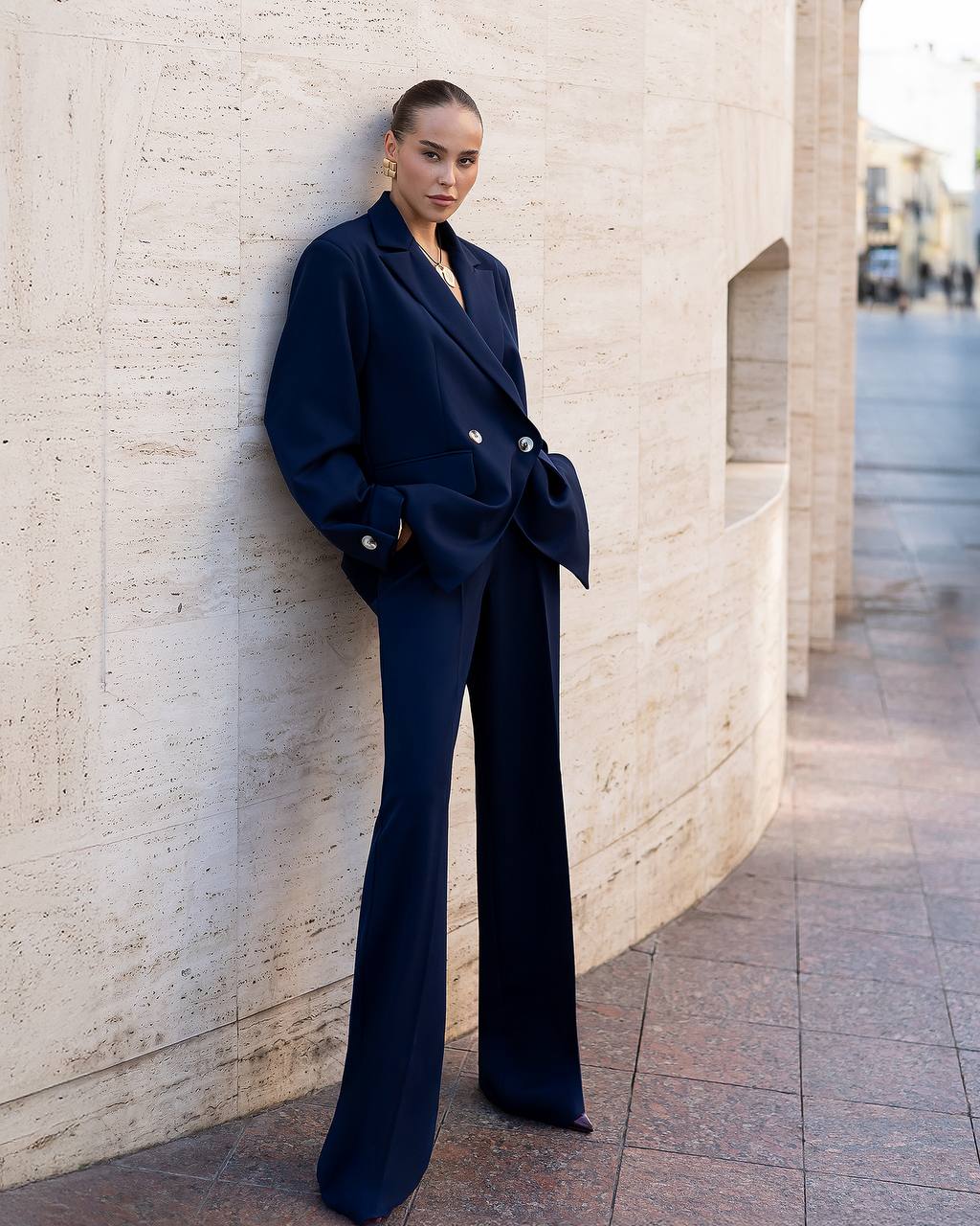 Woman in a navy blue outfit standing against a light-colored wall.