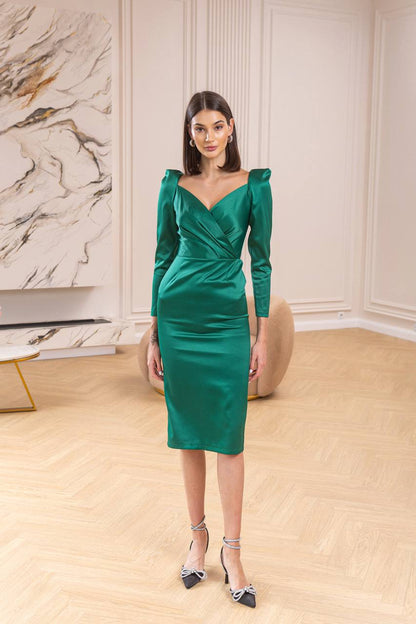 Woman in a green dress standing in a room with marble wall and wooden floor.