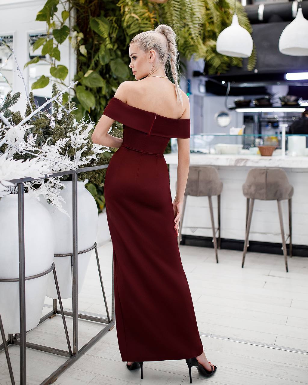 Woman in a burgundy off-shoulder dress standing in a modern indoor setting.