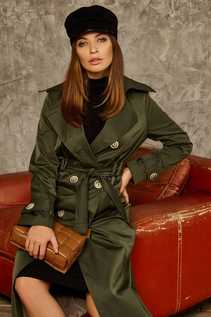 Woman in a green trench coat sitting on a red couch with a textured wall background
