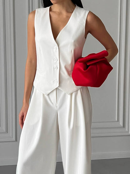 Person wearing a white outfit holding a red clutch against a gray wall.