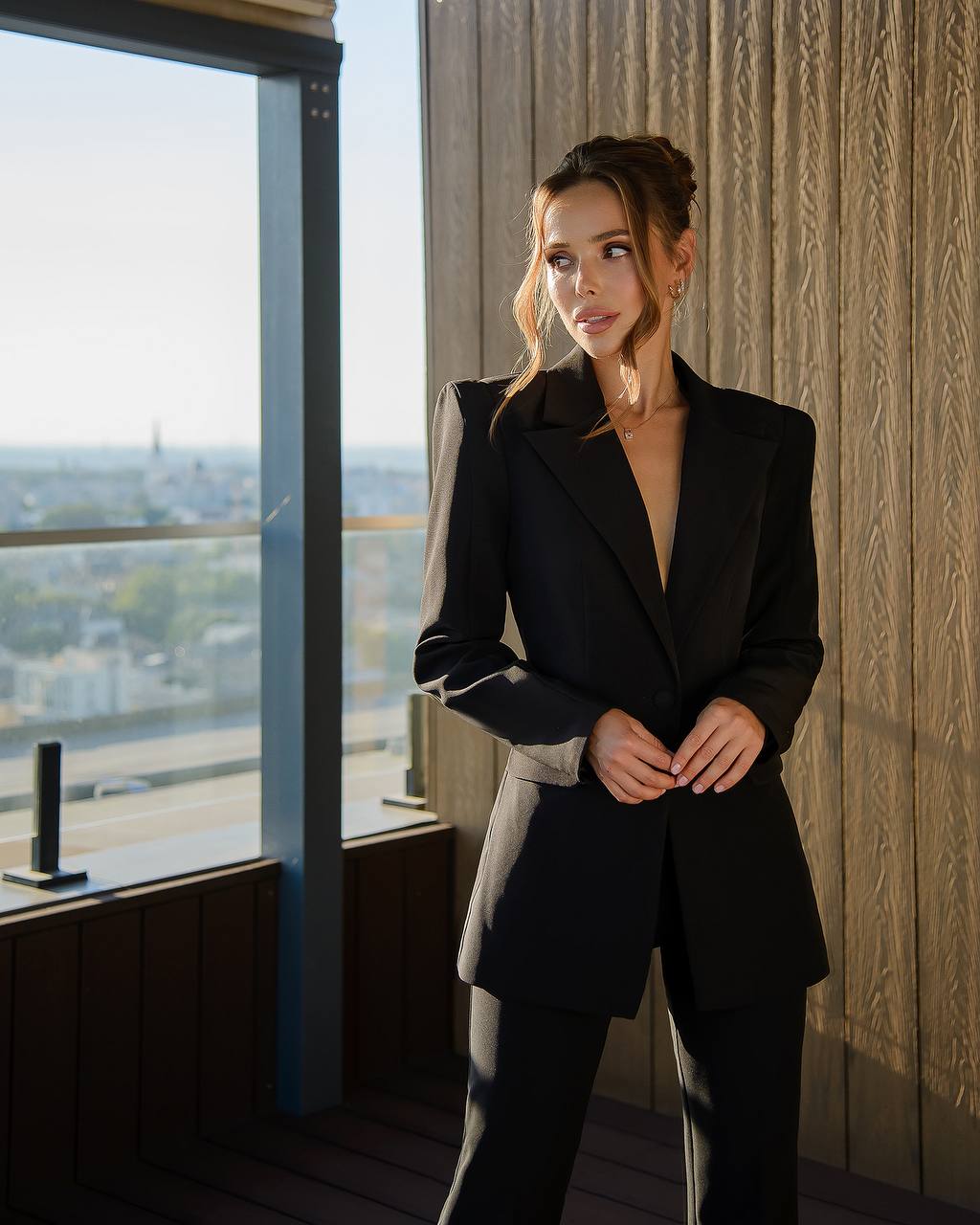 Woman in a black outfit standing by a window with a cityscape view