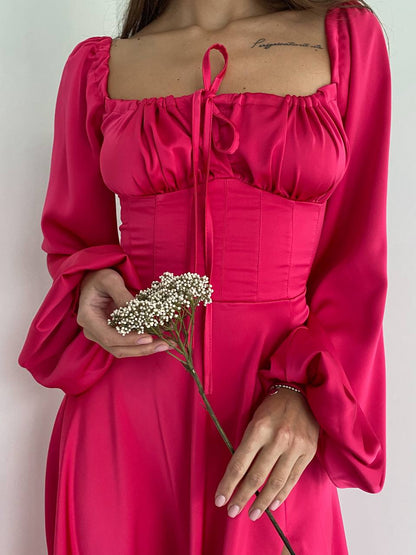 Person wearing a bright pink dress holding a small bouquet of flowers against a plain background