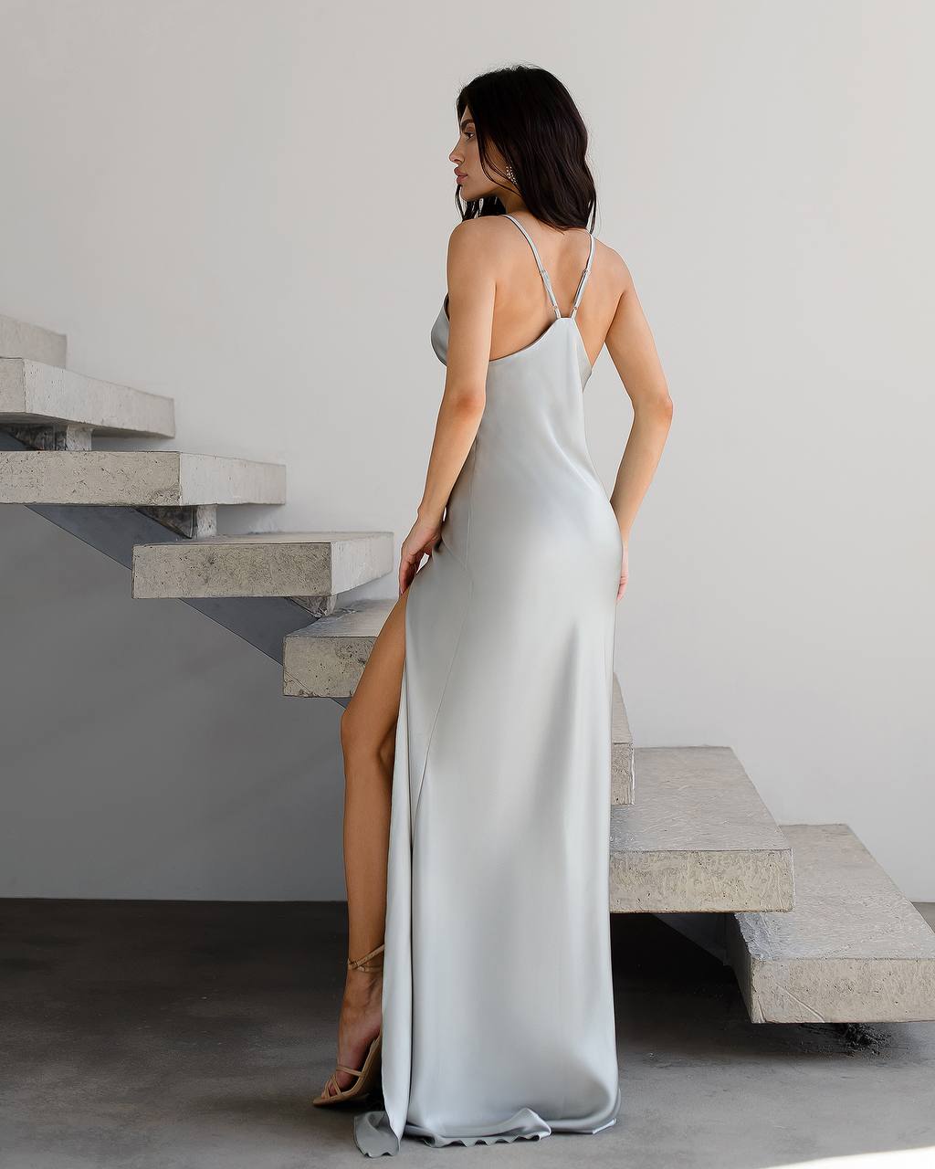 Woman in a light gray slip dress standing on a staircase.