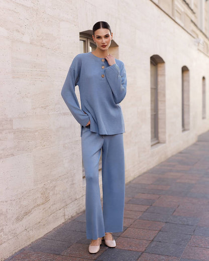 Woman in a blue outfit standing against a beige brick wall.