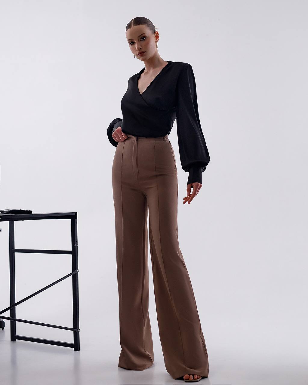 Woman wearing a black top and brown pants on a white background