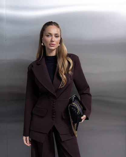 Woman in a dark suit holding a handbag against a neutral background