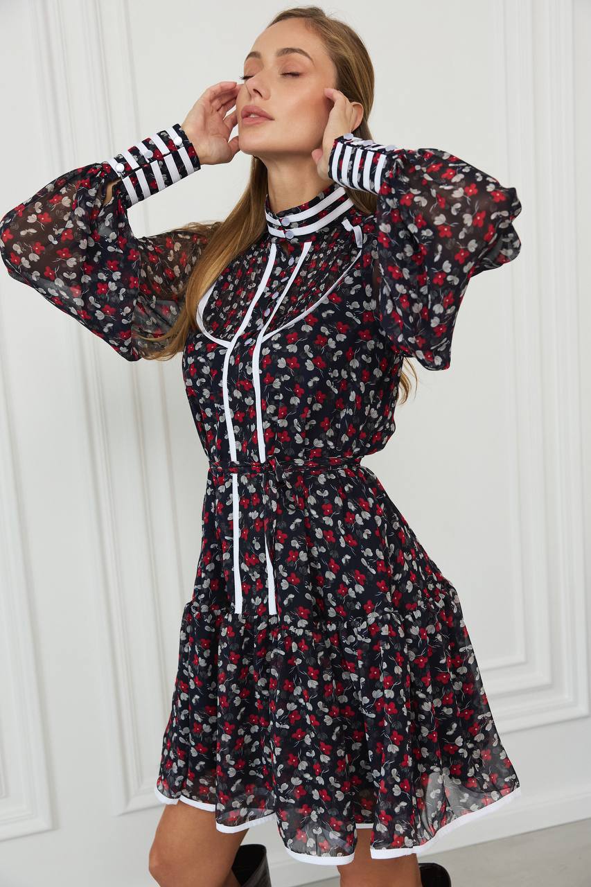 Woman wearing a floral dress with striped cuffs against a white wall