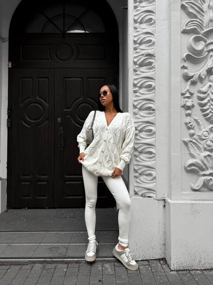 Woman in a white outfit standing in front of a black door with decorative patterns.