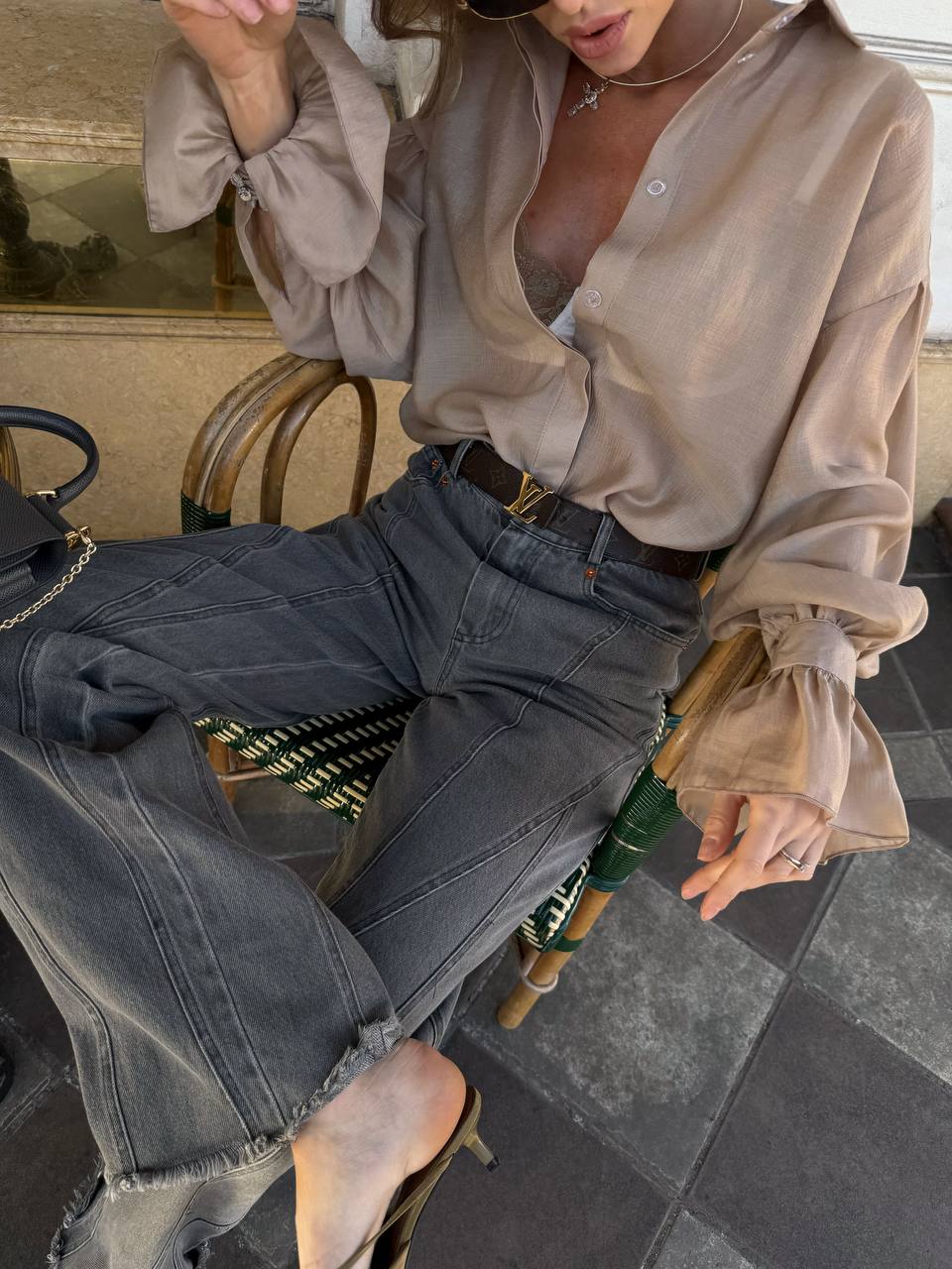 Person wearing a beige blouse and dark jeans sitting on a chair.