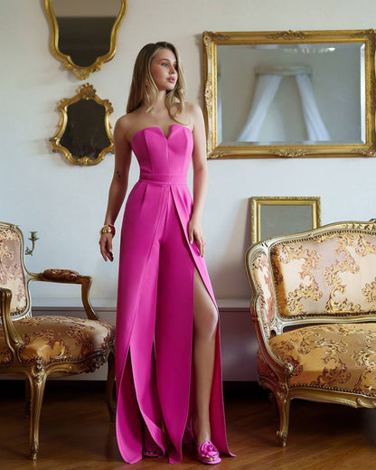 Woman in a pink strapless gown with a high slit standing in an ornate room with gold mirrors and furniture.