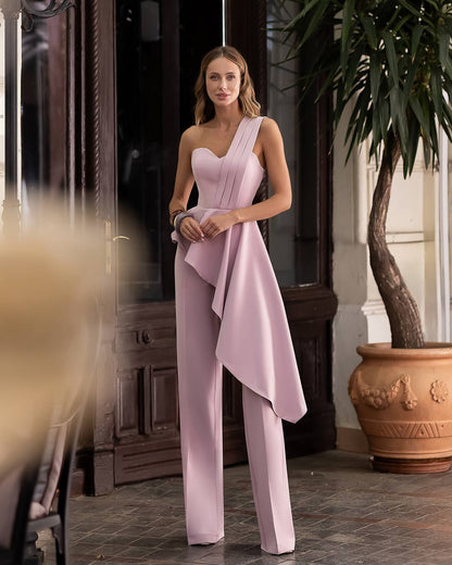 Woman wearing a pink one-shoulder jumpsuit standing indoors with decorative elements.