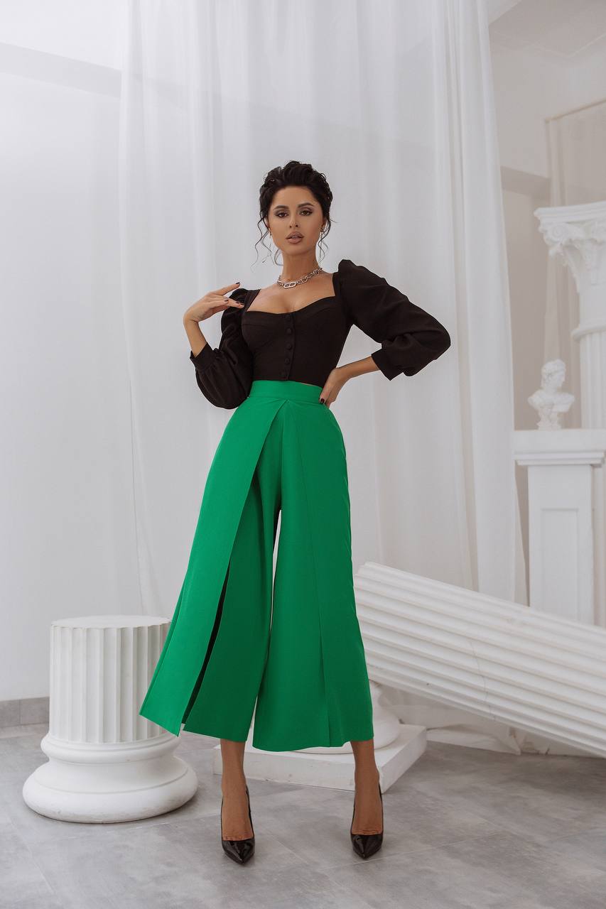Woman wearing a black top and green pants in an elegant interior setting