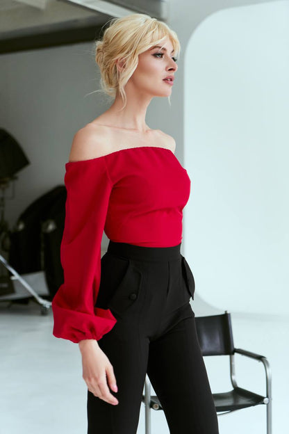 Woman wearing a red off-shoulder top and black pants in an indoor setting.