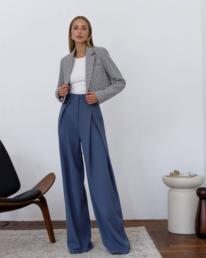 Woman wearing a checkered blazer and blue pants in a minimalistic room.