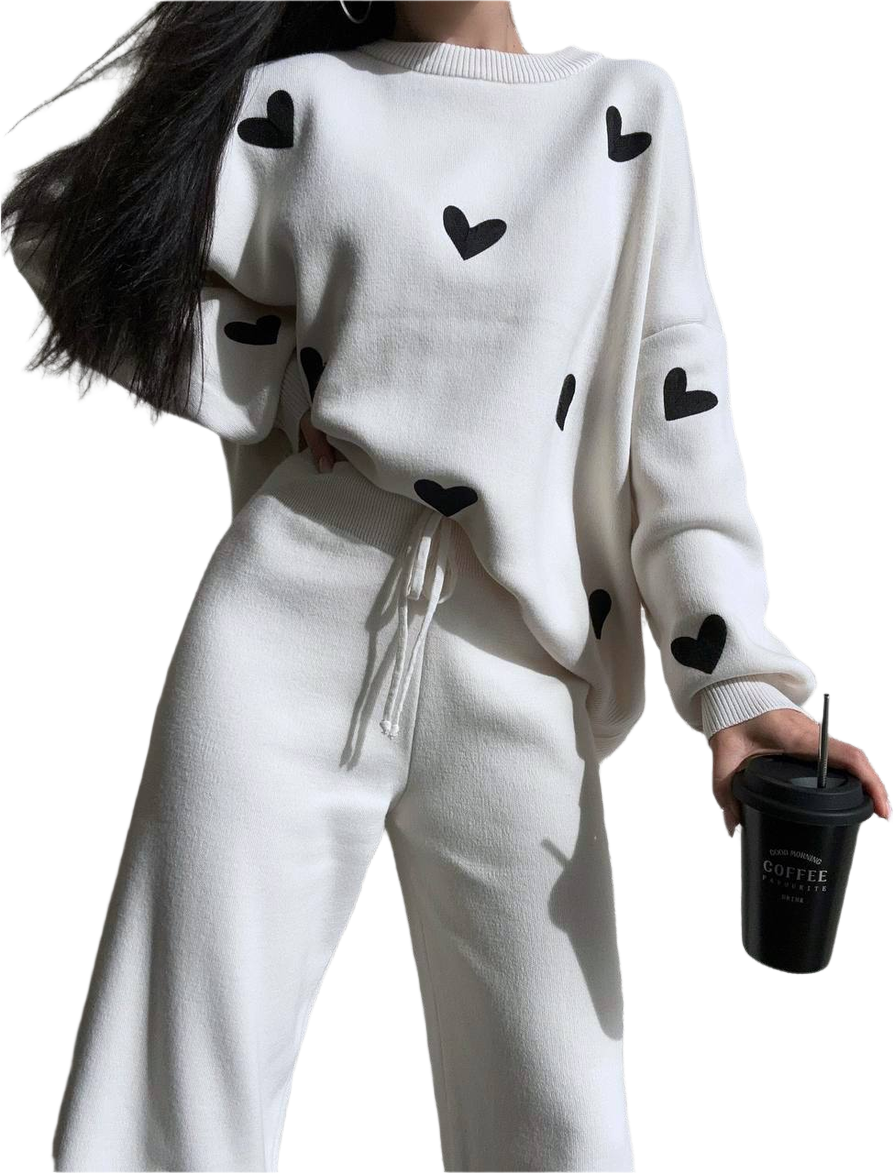 White outfit with black heart patterns worn by a person, holding a black coffee cup.