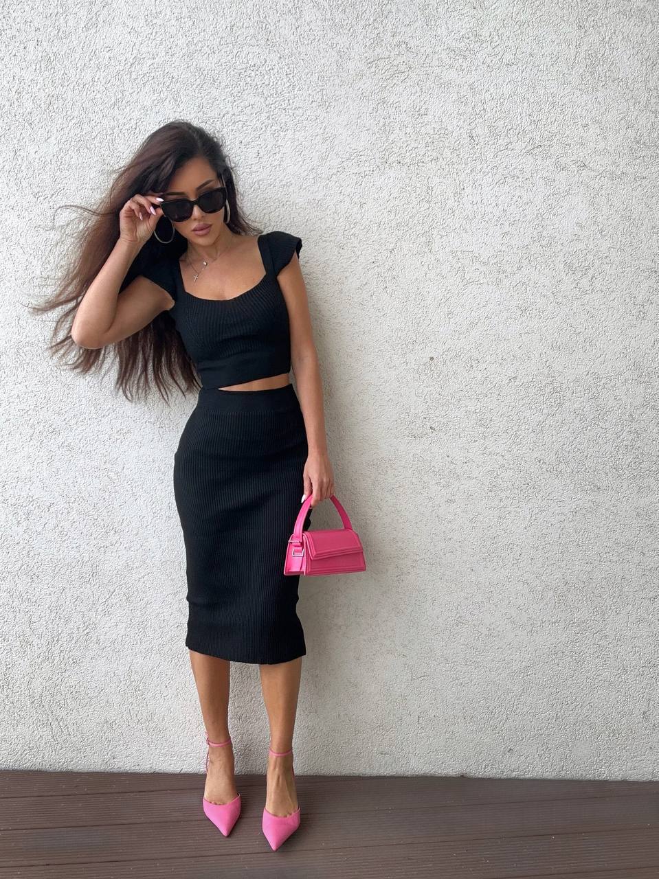 Woman in black outfit with pink handbag against a light gray wall