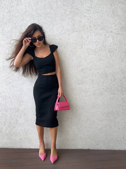 Woman in black outfit with pink handbag against a light gray wall