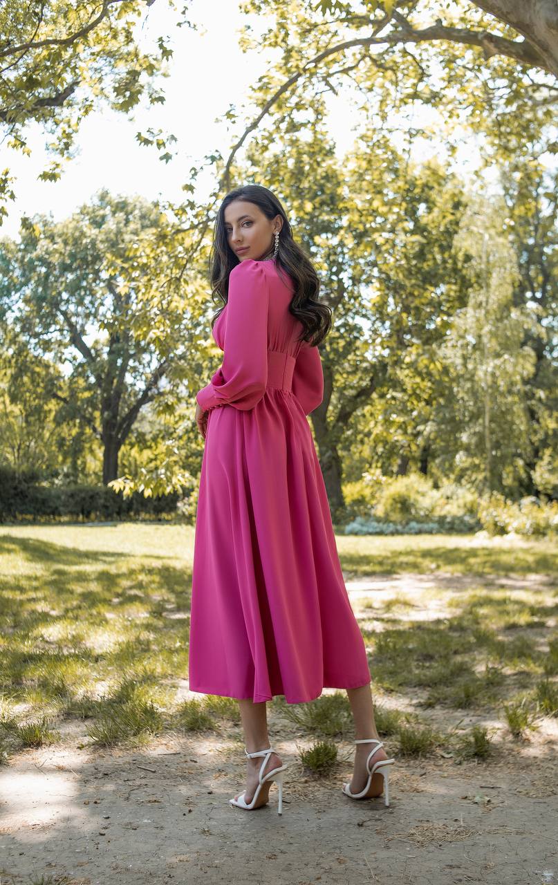 Woman in a pink dress standing in a park with trees and grass in the background