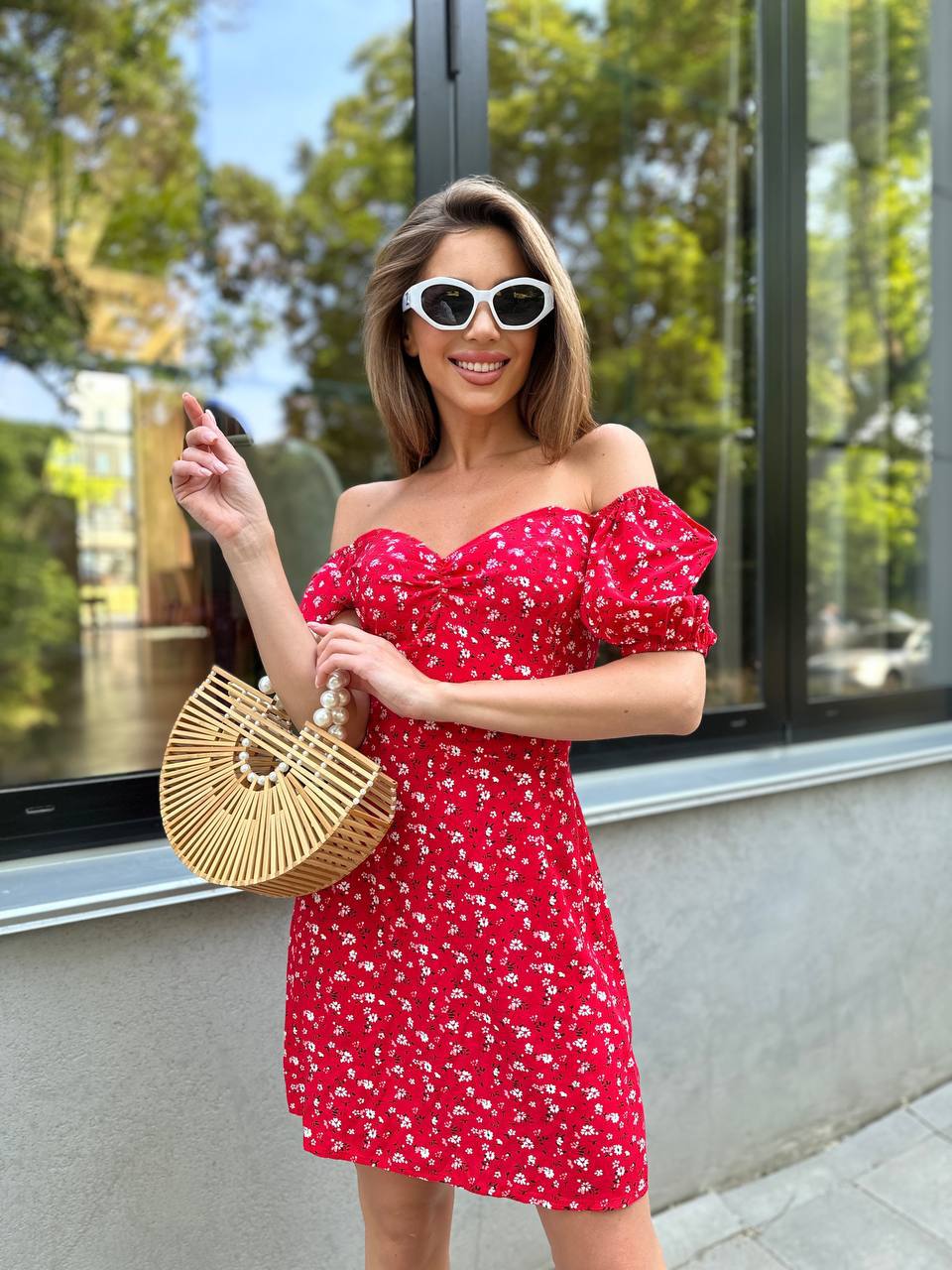 Woman in a red floral dress holding a straw bag outdoors.