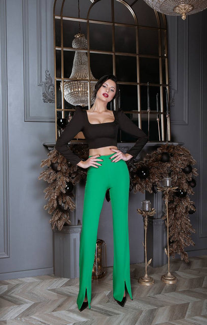 Woman in black top and green pants posing in a decorative room with chandeliers and wreaths.
