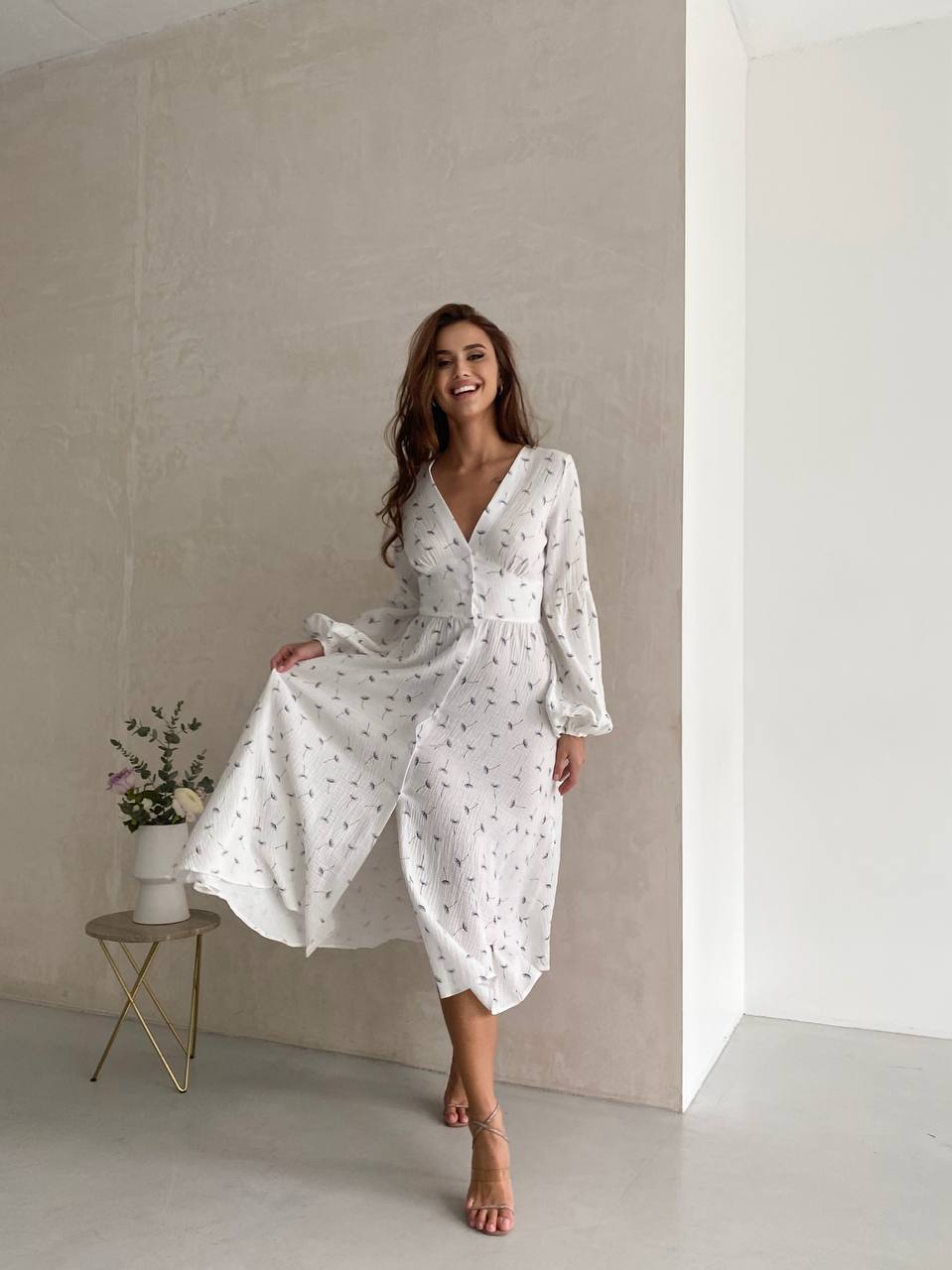 Woman wearing a white dress with a subtle pattern in a minimalistic setting.