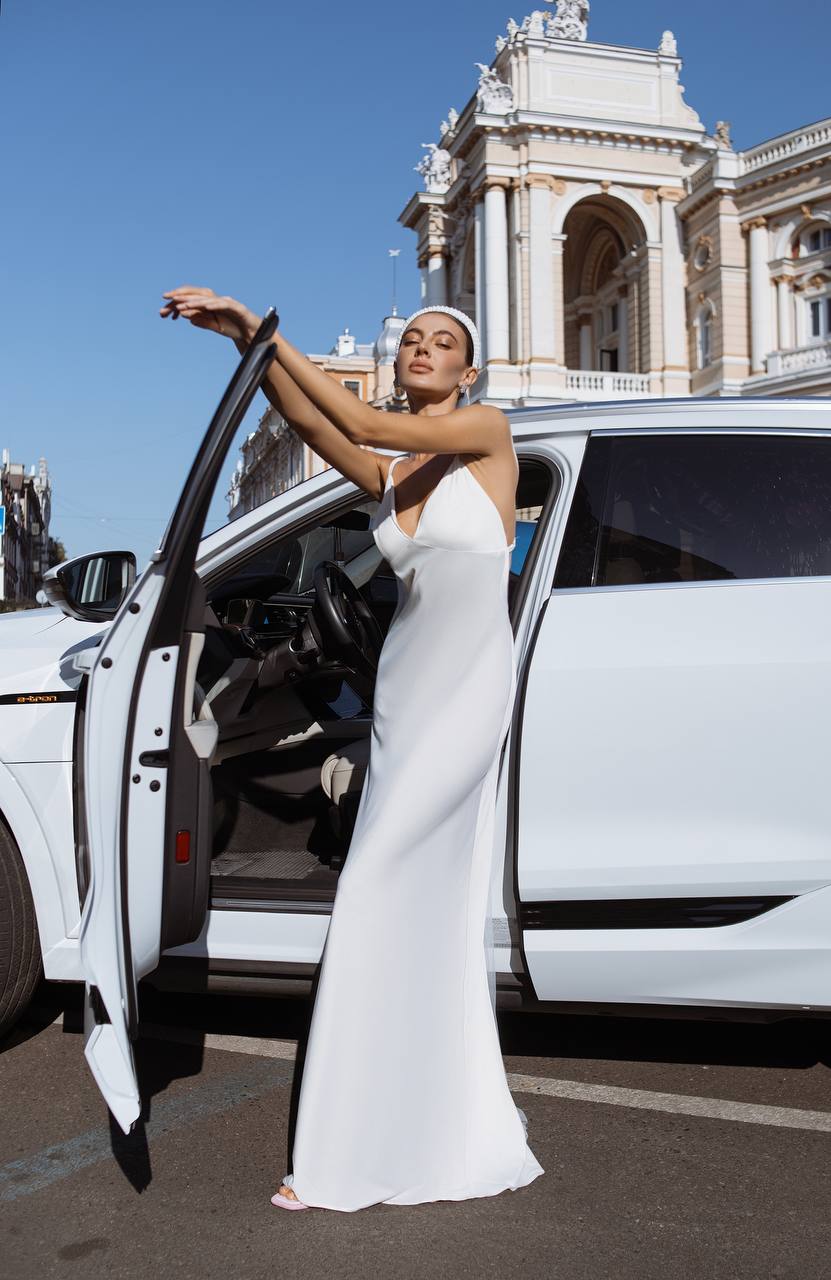 Woman in a white dress stepping out of a white car with a classical building in the background