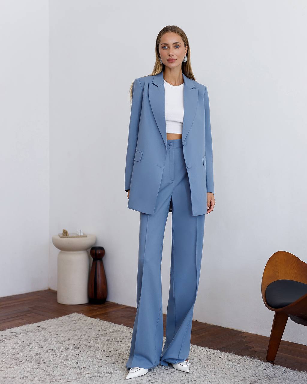 Woman wearing a blue suit standing in a room with a white wall and wooden floor.