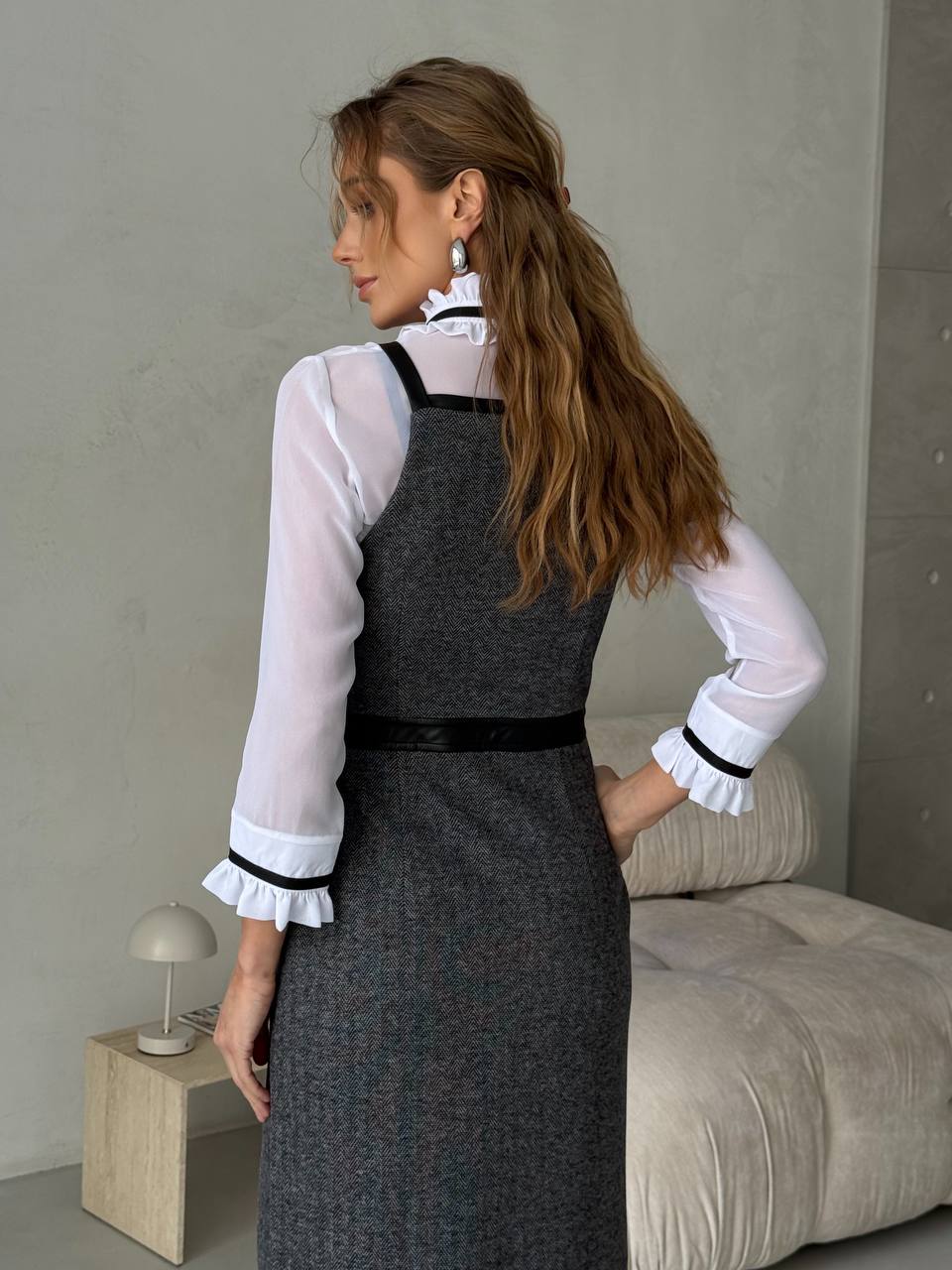Woman wearing a gray dress with a white blouse in a minimalistic room.