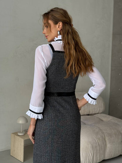 Woman wearing a gray dress with a white blouse in a minimalistic room.