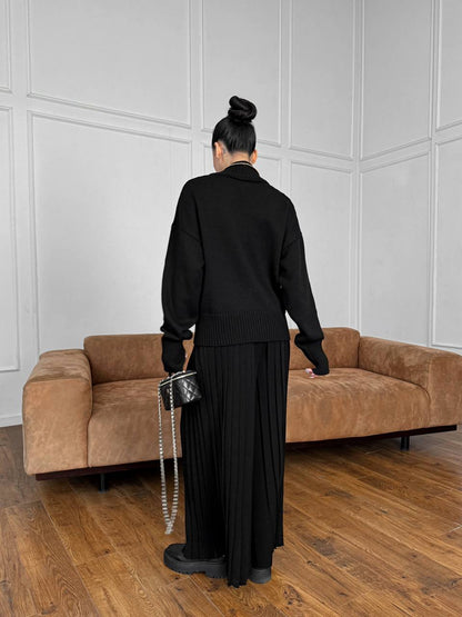 Person in black outfit standing in a room with a brown sofa and white paneled walls.