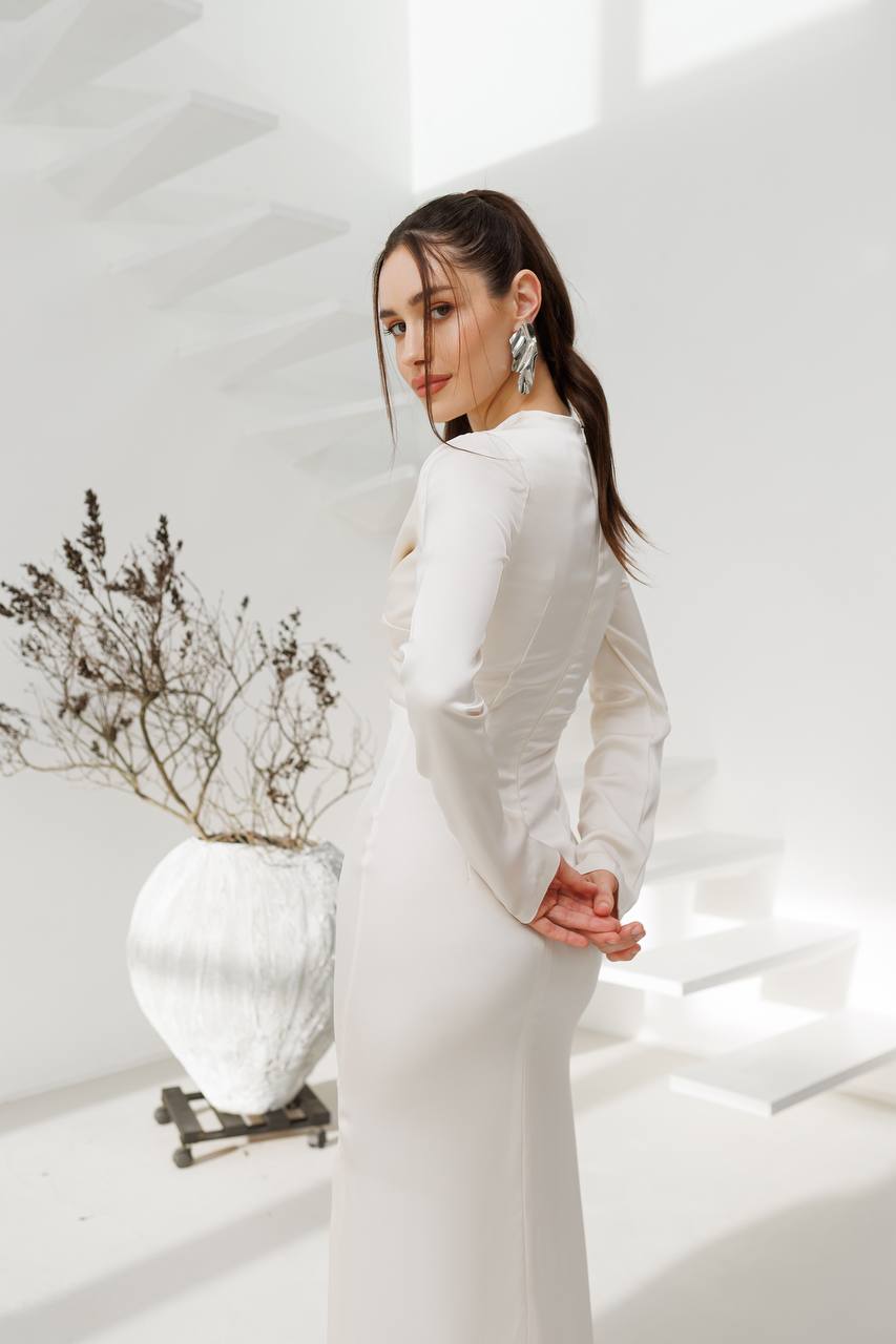 Woman in a white dress standing in a minimalistic room with a plant.