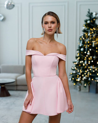 Woman wearing a pink off-shoulder dress in a decorated room with a Christmas tree.
