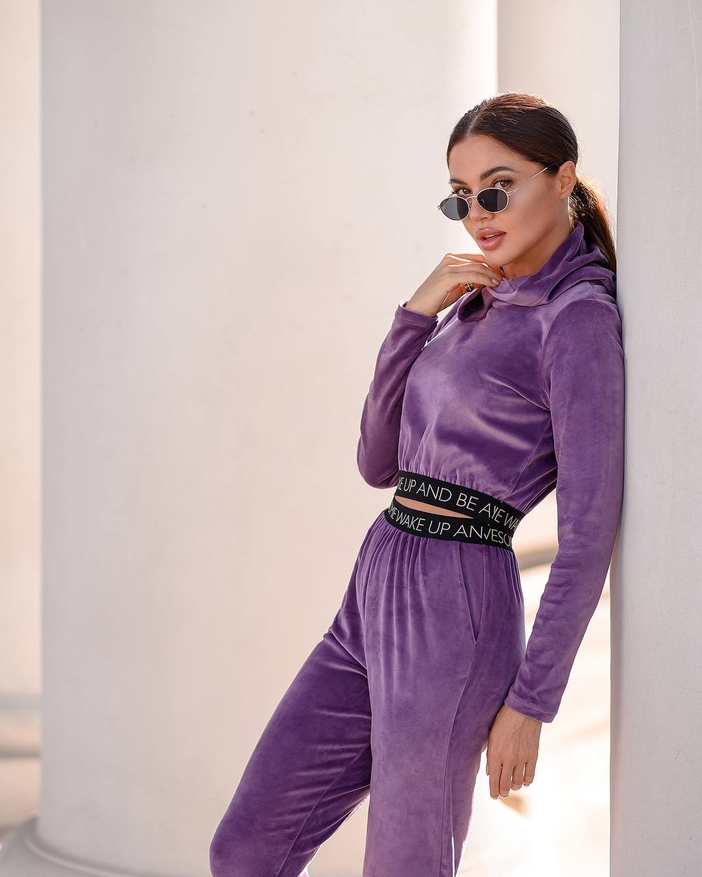 Woman wearing a purple tracksuit with text design, standing against a light-colored wall.
