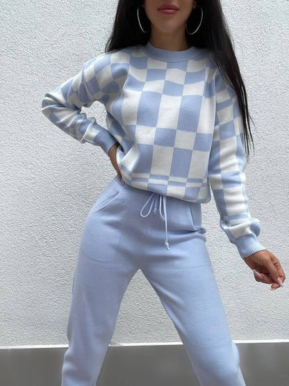 Person wearing a blue and white checkered sweater and pants against a plain background