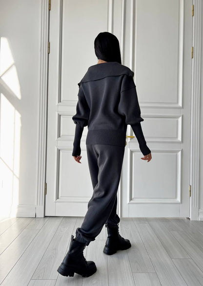 Person wearing a dark outfit in a room with white walls and wooden floor.