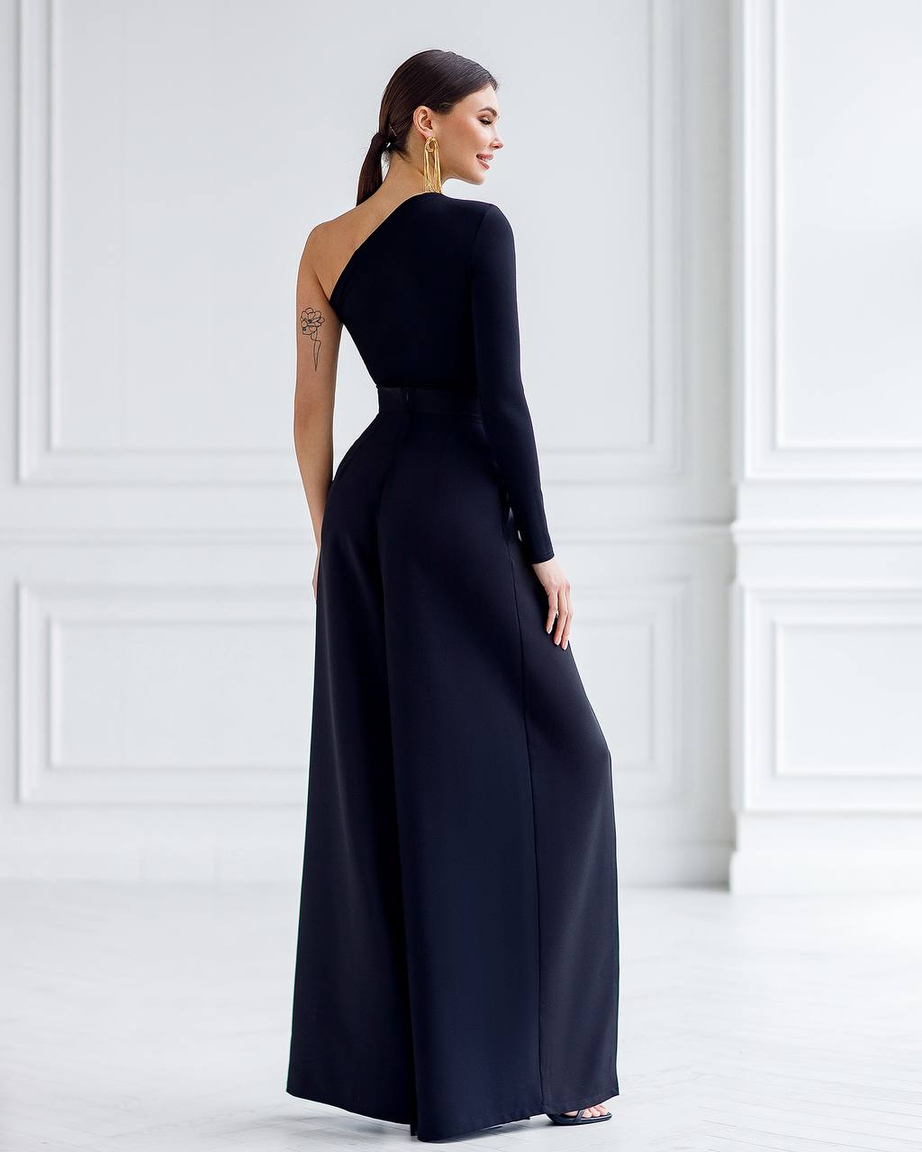 Woman wearing a one-shoulder navy blue gown against a white wall.