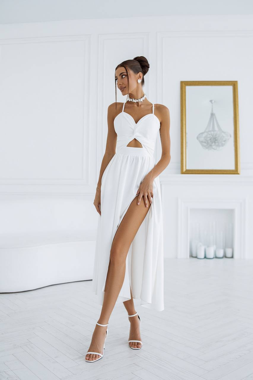 Woman wearing a white dress with a high slit in a minimalistic room.