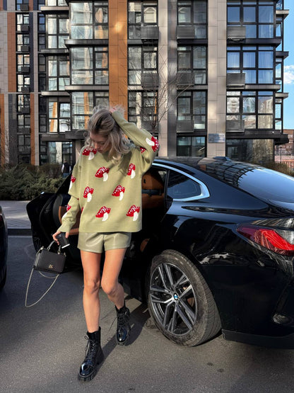 Person wearing a light green sweater with red patterns, black shorts, and black boots standing next to a black car in an urban setting.