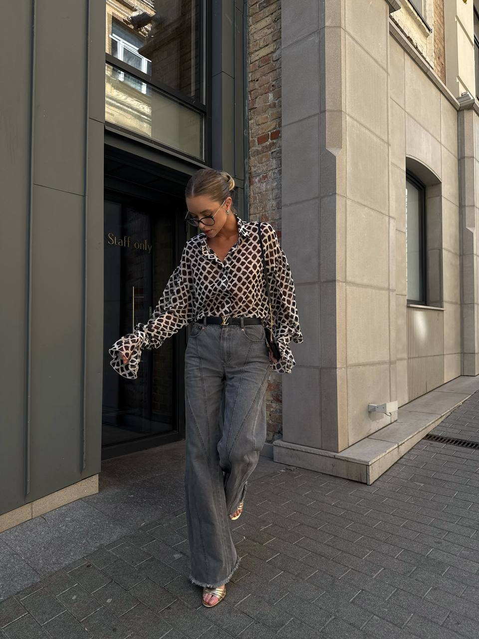 Person wearing a leopard print shirt and gray pants walking outside a building.