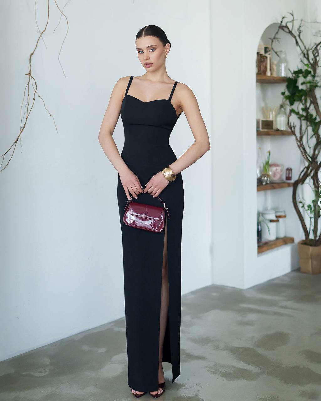 Woman in a black dress holding a red handbag in an indoor setting.
