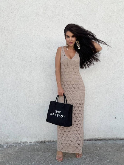 Woman in a patterned dress holding a black bag against a white wall