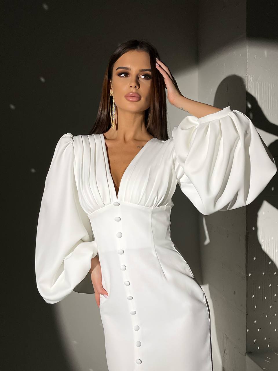 Woman wearing a white dress with puffed sleeves against a dark background